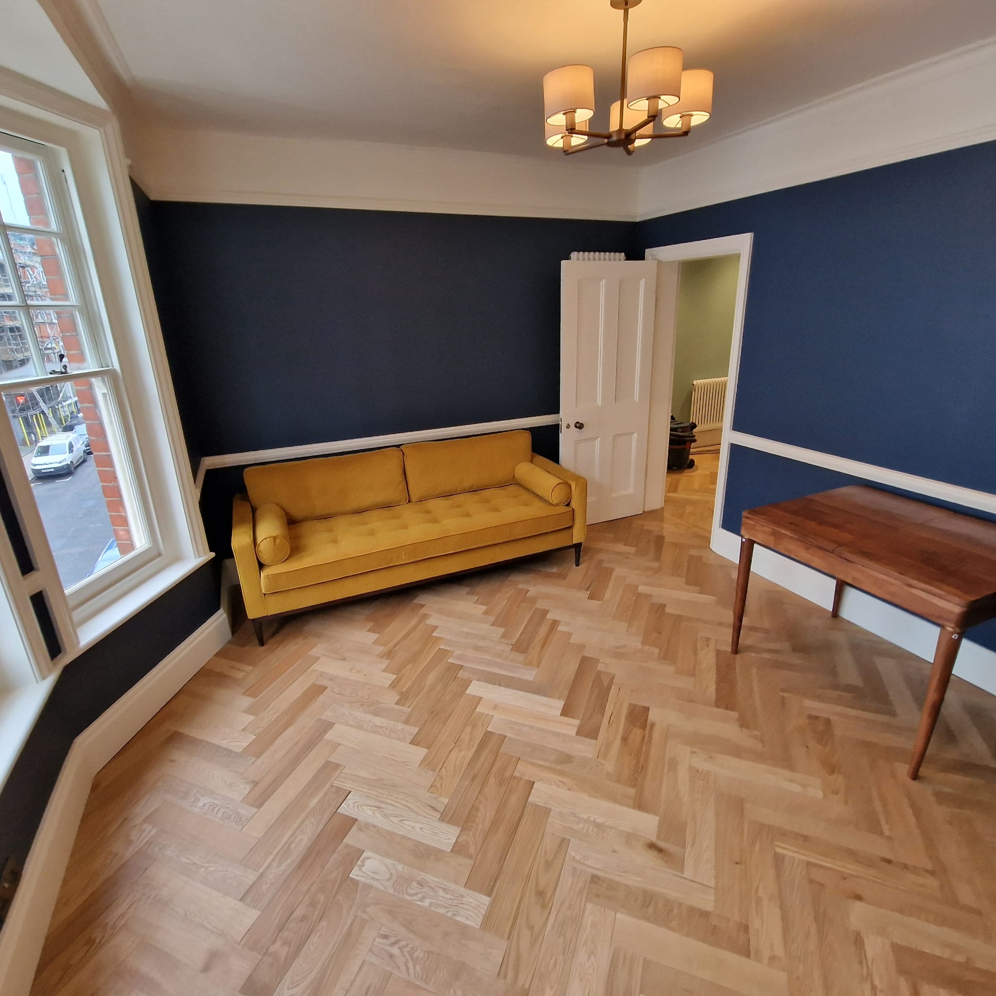Period sitting room with navy walls, herringbone parquet floor and mustard velvet sofa