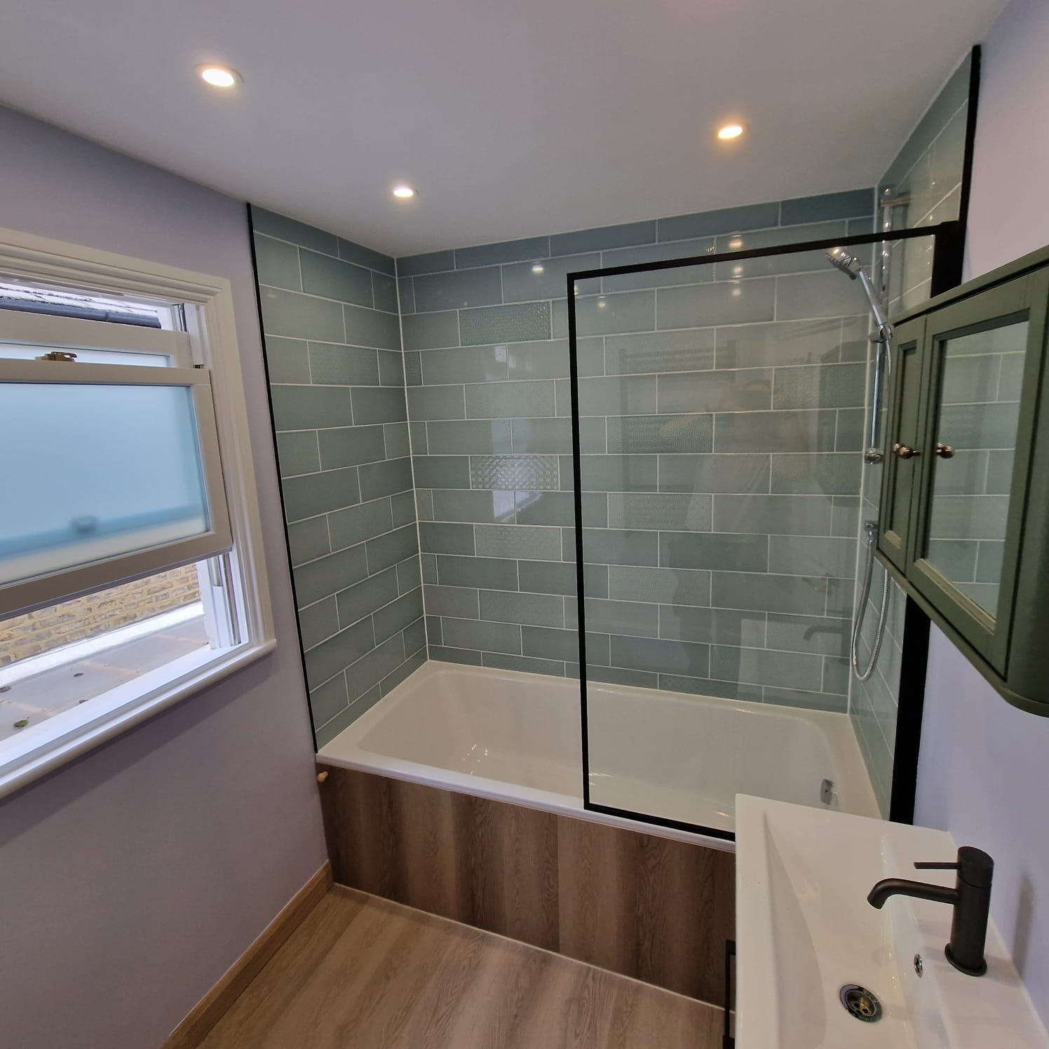 Bathroom with sage subway tiles, black-framed shower screen and engineered wood floor