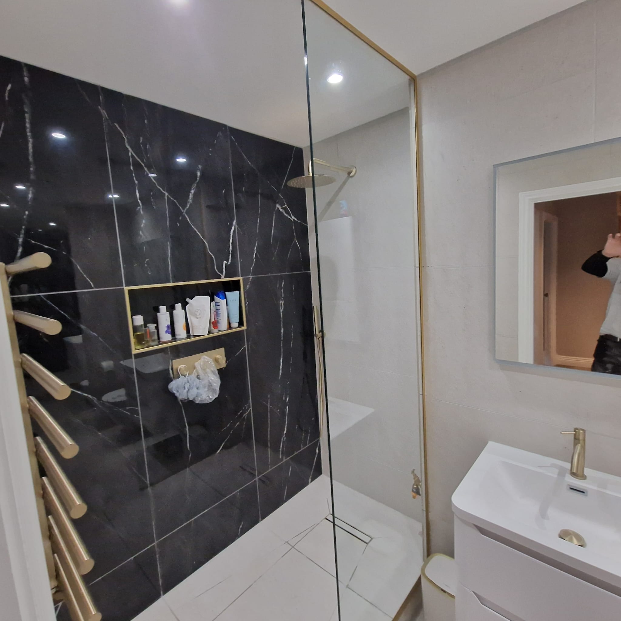 Black marble shower wall with brass niche and brass towel ladder