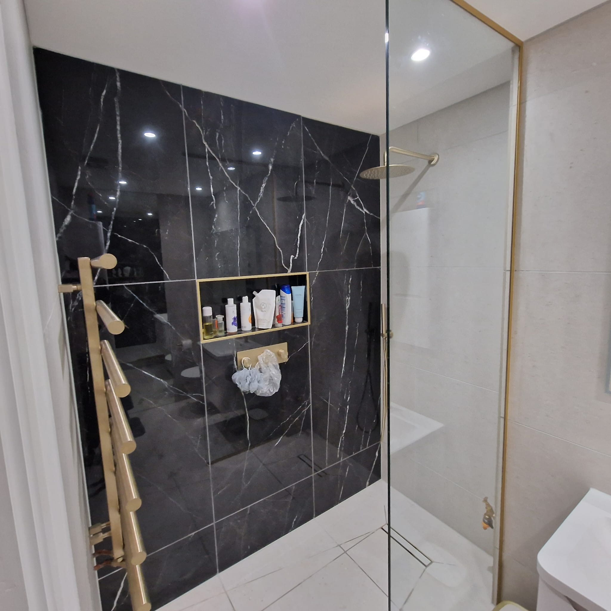 Walk-in shower with black marble effect tiles and brass fixtures